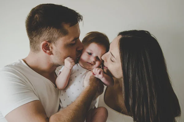 Padres jóvenes sosteniendo pequeño bebé y besándose en fondo blanco —  Fotos de Stock