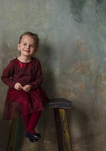 Маленькая девочка в красном платье сидит на деревянной лестнице и улыбается — стоковое фото