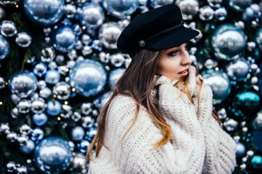  Noel deco 'sunun yanında poz veren kalın kazaklı genç bir kadın.