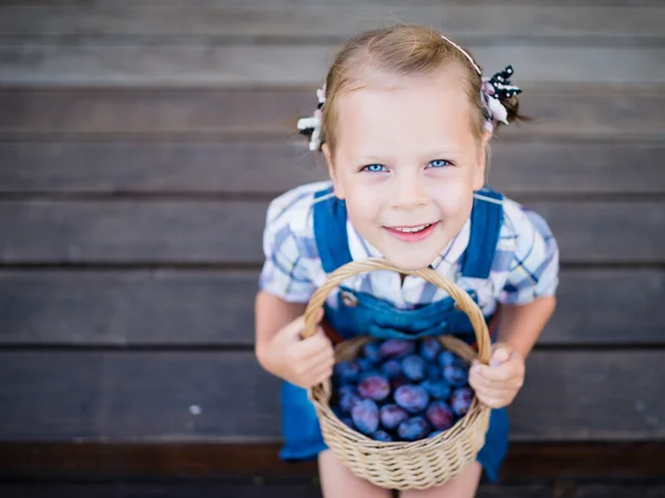 Kind meisje met mand vol pruimen — Stockfoto