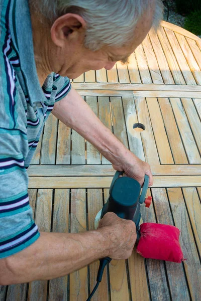 Oude man - timmerman werken met elektrische sander in de tuin Stockfoto