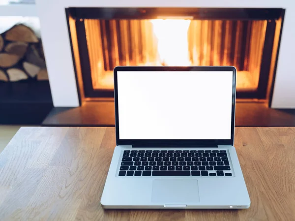 Laptop com tela em branco na mesa de madeira na frente da lareira em chamas — Fotografia de Stock