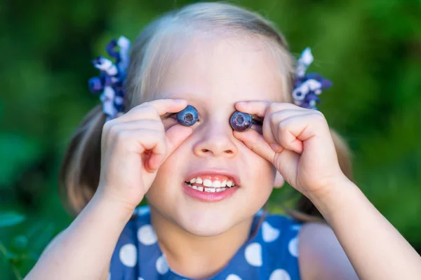 Smiling girl showing blueberries in front of her face — Stock Photo, Image