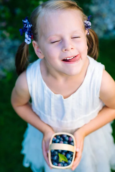 Little girl licking her lips with her eyes closed holding a bask — Stock Photo, Image