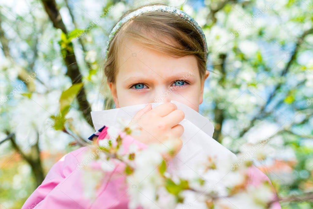Allergy. Little girl is blowing her nose near spring tree in bloom