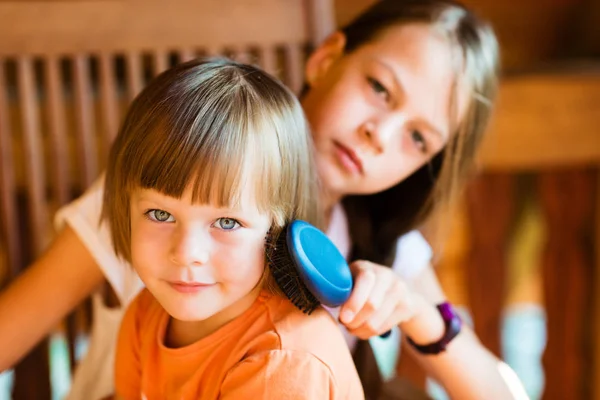 Pretty girl combing hair of younger sister — Stock Photo, Image