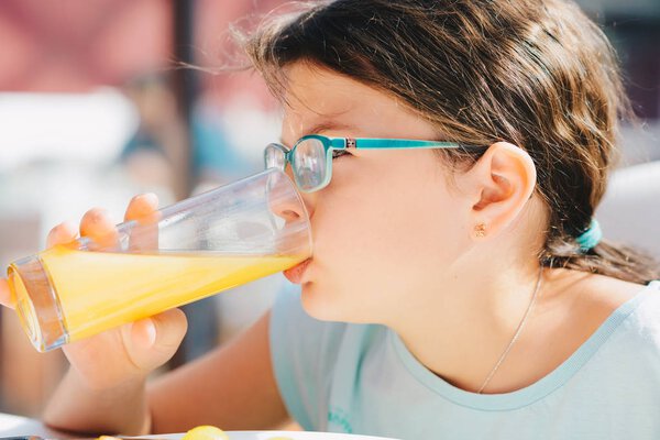 Portrait of a pretty child girl holding glass with tasty orange 