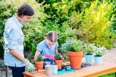 Anne ve kızı bahçedeki saksılara çiçek dikiyor. Birlikte çalışma, ailesiyle vakit geçirme kavramı.