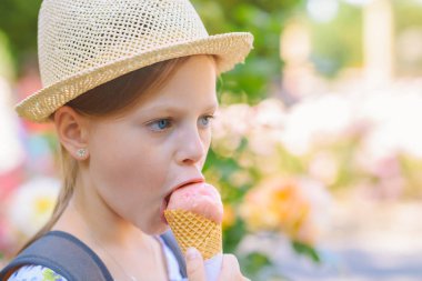 Hasır şapkalı küçük kız güneşli bir yaz gününde külahta dondurma yiyor.