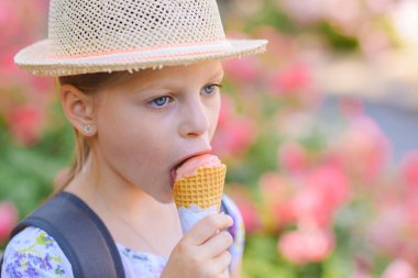 Hasır şapkalı küçük kız güneşli bir yaz gününde külahta dondurma yiyor.