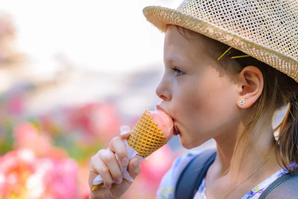 Hasır şapkalı küçük kız güneşli bir yaz gününde külahta dondurma yiyor.