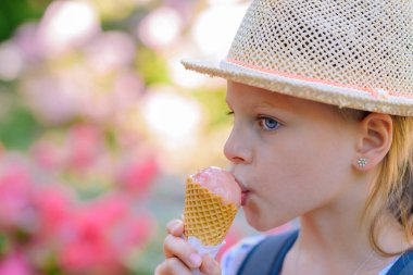Hasır şapkalı küçük kız güneşli bir yaz gününde külahta dondurma yiyor.