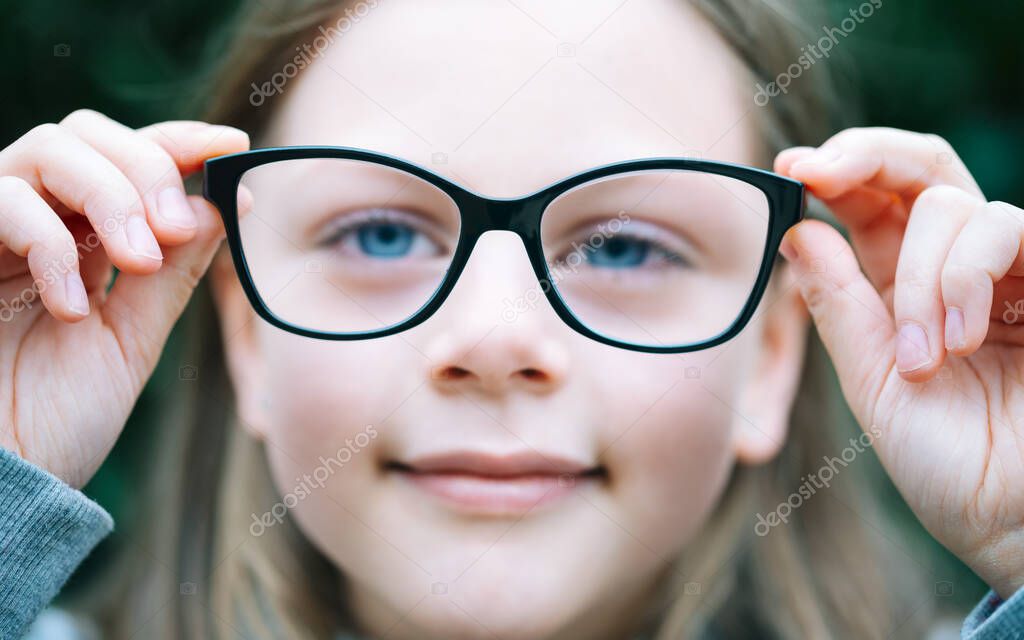 Closeup portrait of little girl  with myopia correction glasses. Girl is holding her eyeglasses right in front of camera with two hands - focus on glasses - shallow depth of field