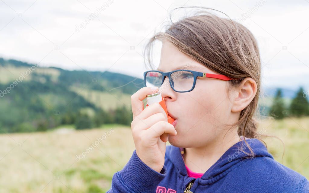 Girl having asthma using asthma inhaler outdoors - shallow depth of field