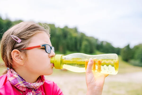 山の旅の間に緑の水のボトルからガラス飲料水を持つ女の子 — ストック写真