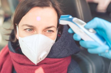 Sıcaklık kontrol noktası - antivirüs maskeli arabanın direksiyonundaki kadın sıcaklık ölçümüne tabi tutuluyor. Coronavirus kavramı - kısıtlamalar, karantina, izolasyon