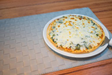 Peynirli ve ıspanaklı İtalyan pizzası ahşap arka planda.