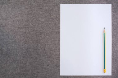 Gri kumaş zemin üzerinde kalem bulunan boş kağıdın üst görünümü