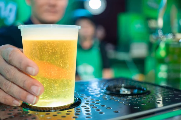 Close up of a male bartender dispensing draught beer in a pub, holding a plastic glass on the automatic fill beer machine