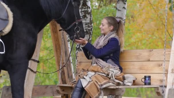 Girl sitting on a bench among the birch trees in the autumn with a horse — Stock Video