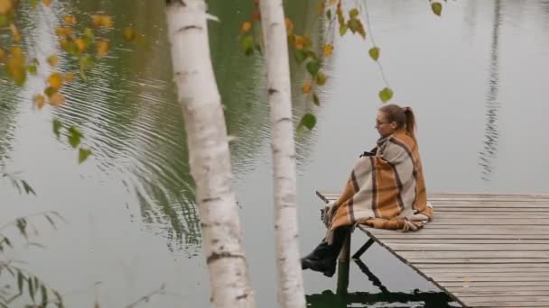 Femme fille assis sur banc en bois sous saule branche mouvement dans le vent près du lac — Video