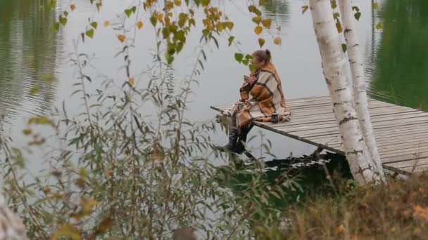 Woman girl sit on wooden bench under willow tree branch move in wind near lake — Stock Video