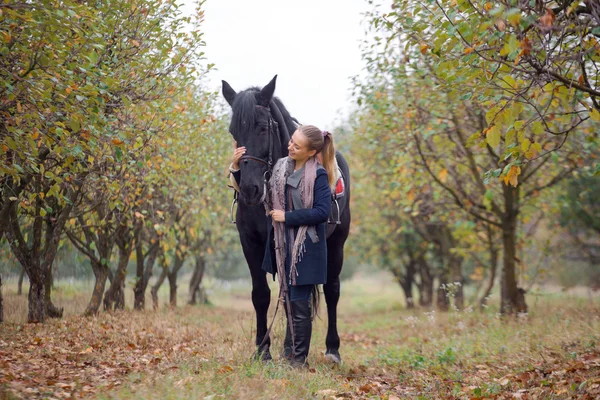 Стильная девушка в шапке-ушанке с лошадью, гуляющая по осеннему лесу, деревенский стиль — стоковое фото