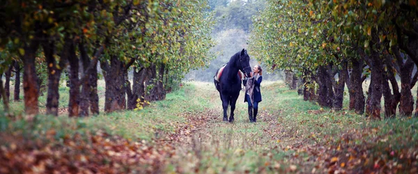 Beautiful stylish girl in a cowboy hat with a horse walking in the autumn forest, country style — Stock Photo, Image
