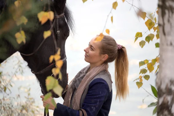Девушка с черной лошадью осенью под березой — стоковое фото