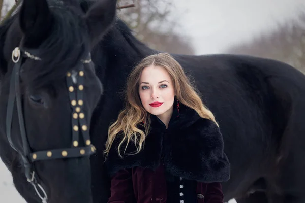 Beautiful woman with a black horse in winter — Stock Photo, Image