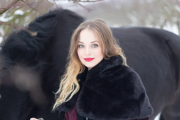 Hermosa mujer con un caballo negro en invierno — Foto de Stock