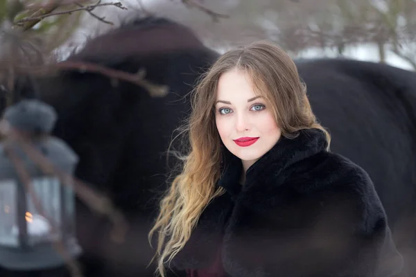 Hermosa mujer con un caballo negro en invierno — Foto de Stock