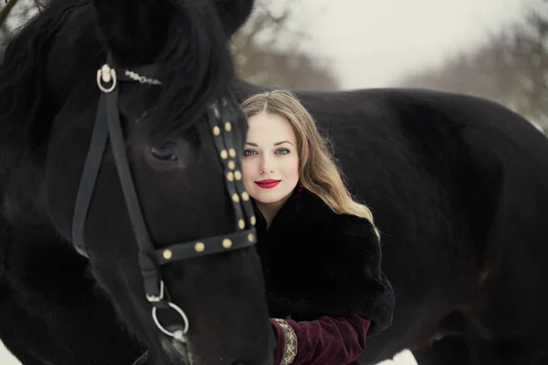 Девушка в темной одежде с черной лошадью — стоковое фото