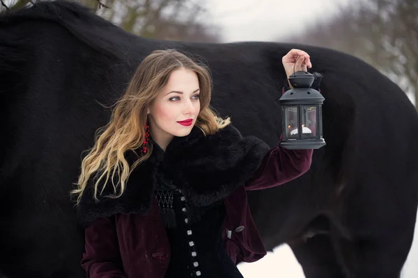 Chica en ropa oscura con un caballo negro — Foto de Stock