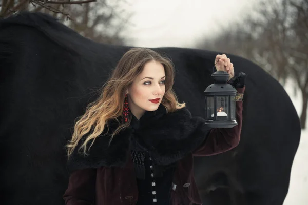 Chica en ropa oscura con un caballo negro — Foto de Stock