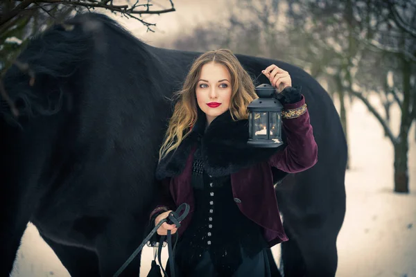 Chica en ropa oscura con un caballo negro — Foto de Stock