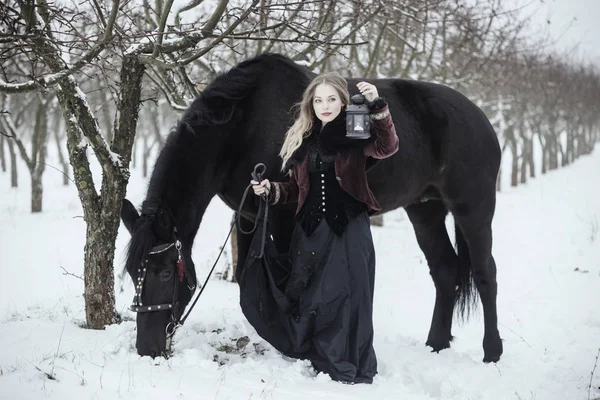 Dívka v tmavých šatech s černým koněm — Stock fotografie