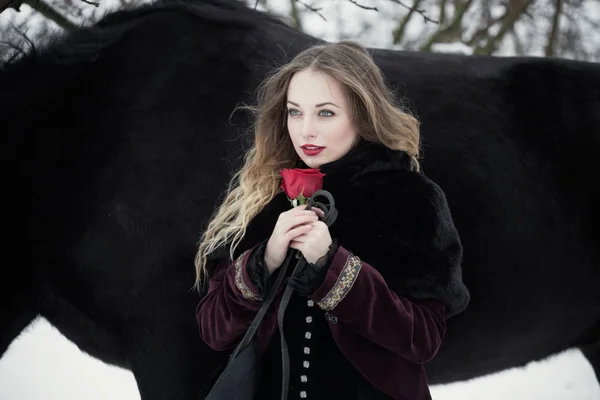 Bela mulher com um cavalo preto no inverno — Fotografia de Stock