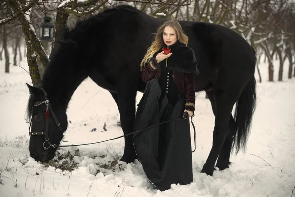 Schöne Frau mit einem schwarzen Pferd im Winter — Stockfoto