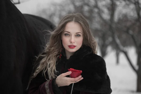 Mujer en un vestido oscuro con una rosa roja en invierno — Foto de Stock