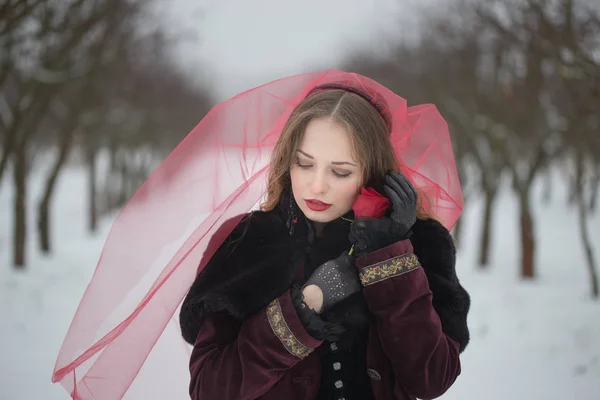 Flicka i en röd slöja på snön på vintern — Stockfoto