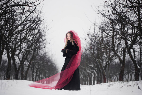 Girl in a red veil on the snow in the winter.
