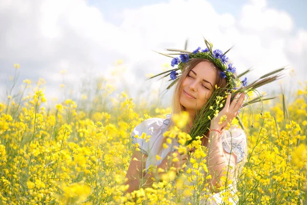 黄色開花フィールドで、彼女の頭の上のカラフルな花の花輪を持つ少女 — ストック写真