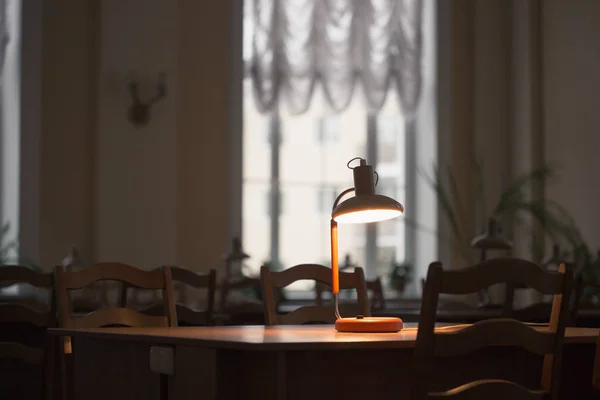 Lendo na mesa com uma lâmpada na biblioteca — Fotografia de Stock