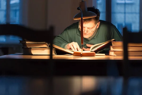 Man reading a book in the library under the lamp — Stock Photo, Image