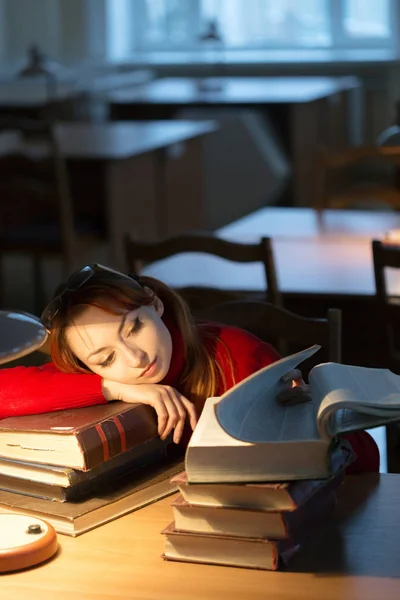 Menina lendo um livro na biblioteca sob a lâmpada — Fotografia de Stock