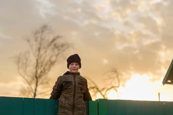 O rapaz está sentado na cerca ao pôr-do-sol — Fotografia de Stock