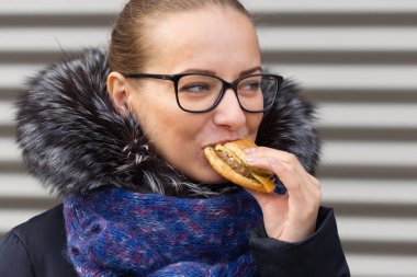 Güzel kız hevesle bir hamburger sokakta yiyor.
