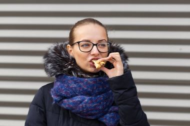 Güzel kız hevesle bir hamburger sokakta yiyor.