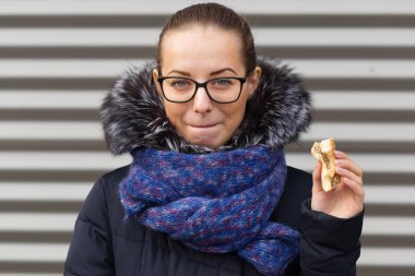 Güzel kız hevesle bir hamburger sokakta yiyor.